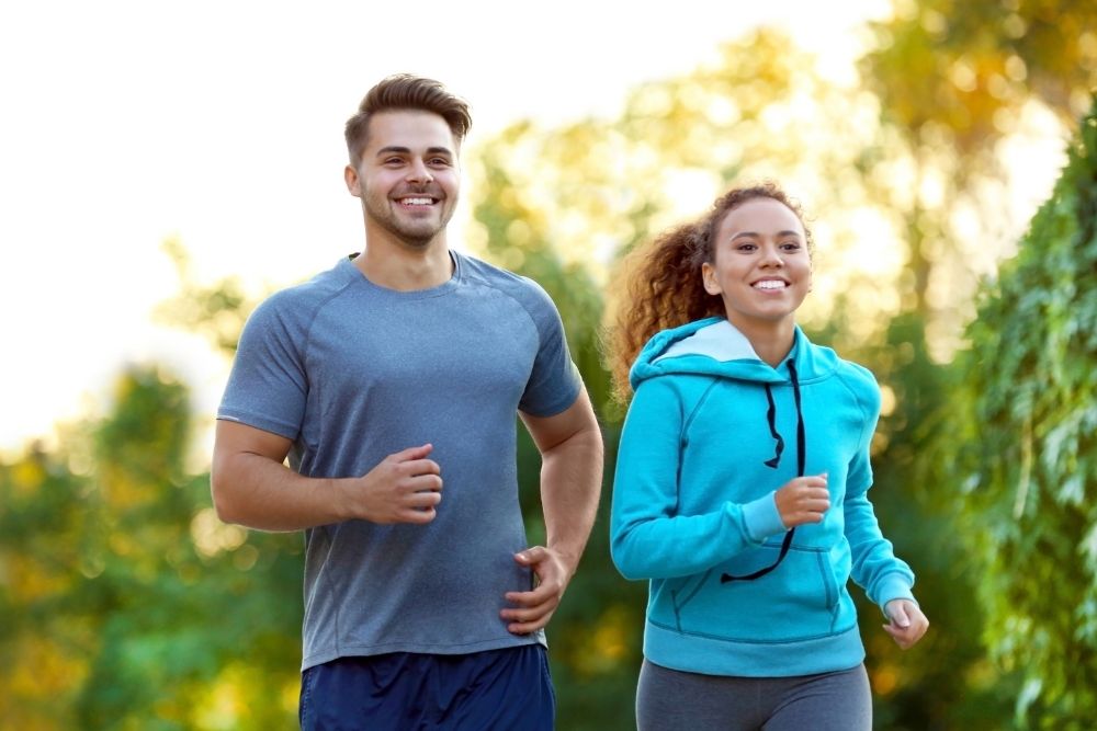 Man and woman happily running outdoors, showing the benefits of healthy lifestyle habits and improved wellness