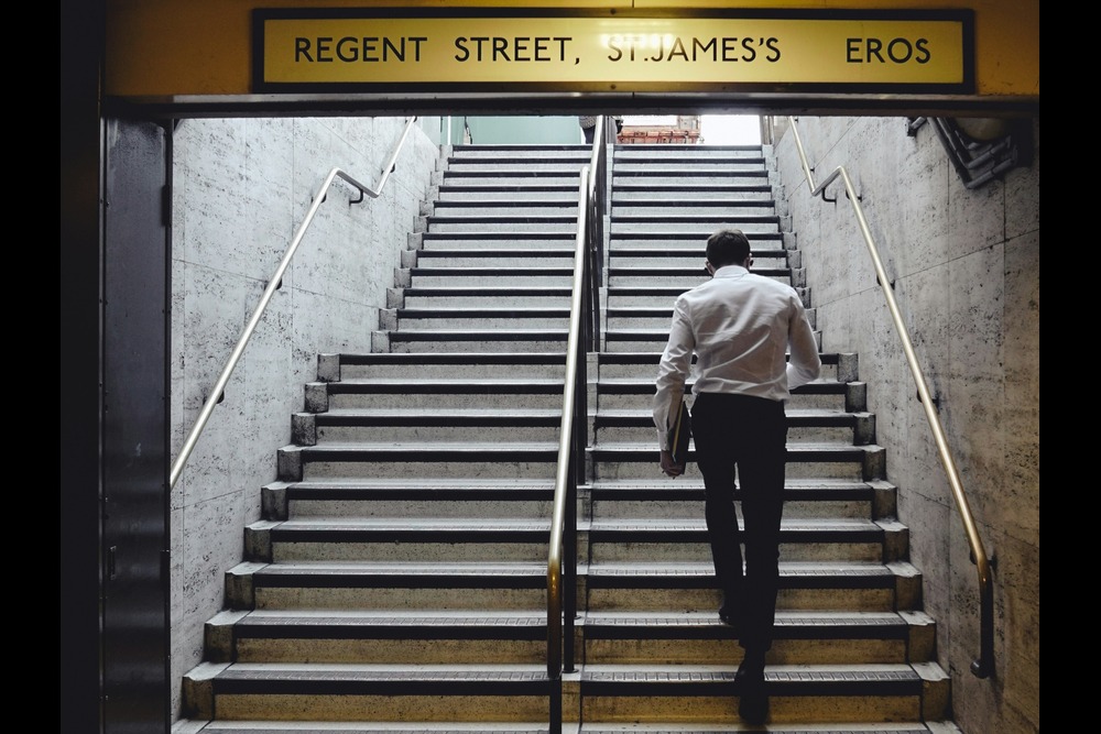 Man climbing stairs on his way to work, demonstrating how daily movement can be an effective exercise for staying active.