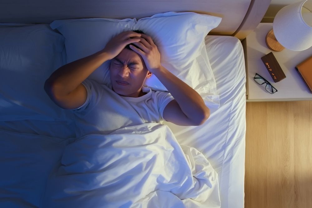 Man lying awake in bed, showing how poor sleep can slow metabolism