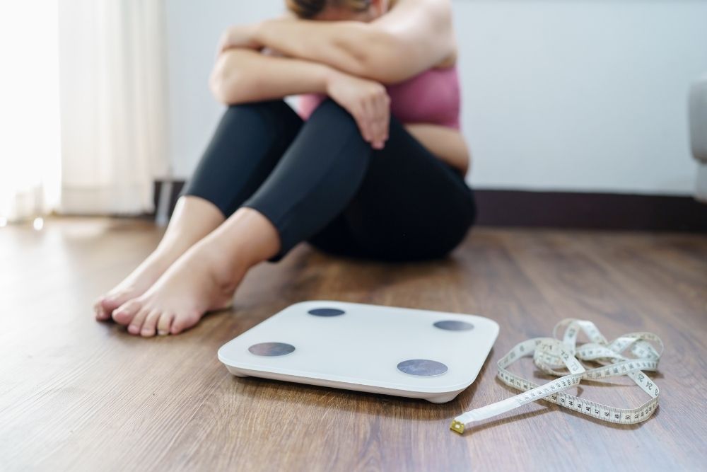 An upset woman with a scale and tape measure, showing the frustration of relying solely on numbers in health and nutrition.