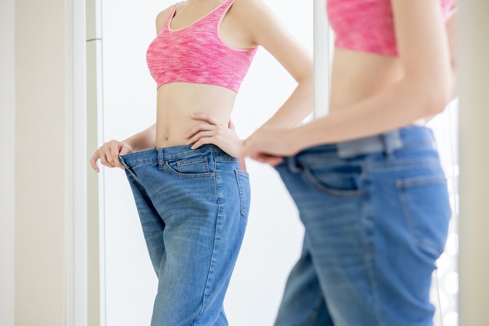 A woman in loose jeans seeing progress that isn't reflected by traditional numbers in health and nutrition.
