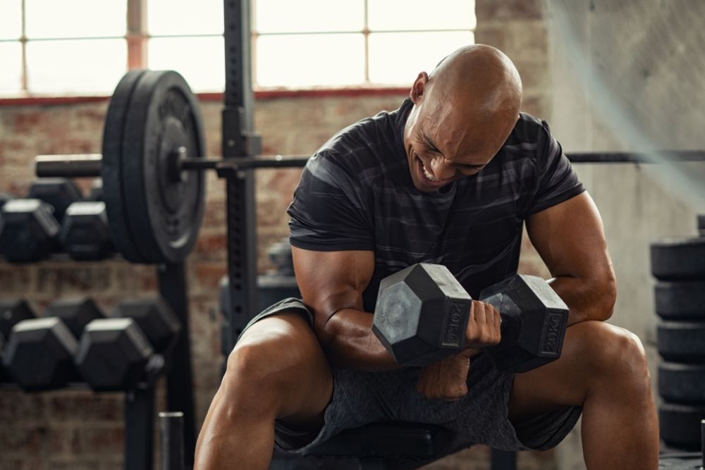 A man lifting heavy dumbbells to demonstrate long-term strength achieved through fundamentals rather than creatine.