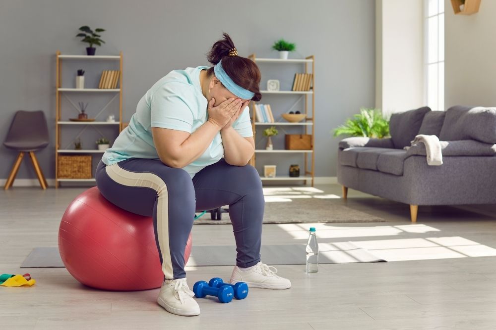 A frustrated woman in workout clothes sitting on a gym ball, representing the mental challenges many face when they start their fitness journey.