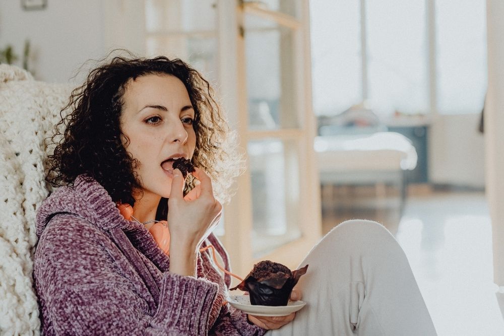 A woman eating a muffin, illustrating the difficulty of breaking a sugar addiction due to harsh withdrawal symptoms.