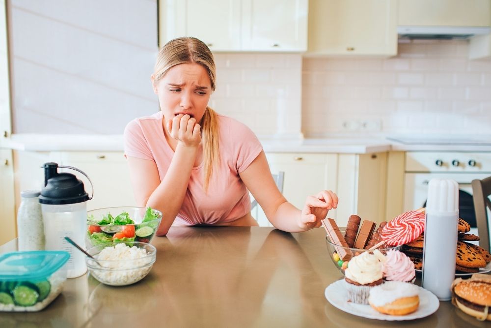 A woman tempted by chocolate over salad, showing the personal responsibility needed to overcome sugar addiction.