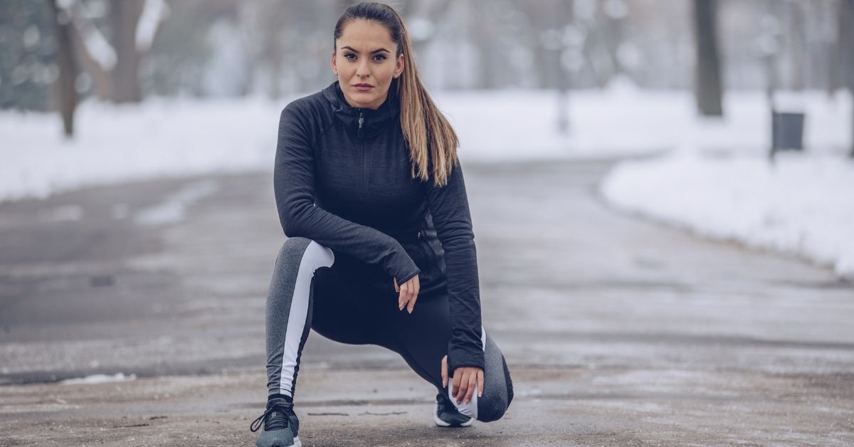 A woman performing outdoor stretches to improve her winter fitness foundation.