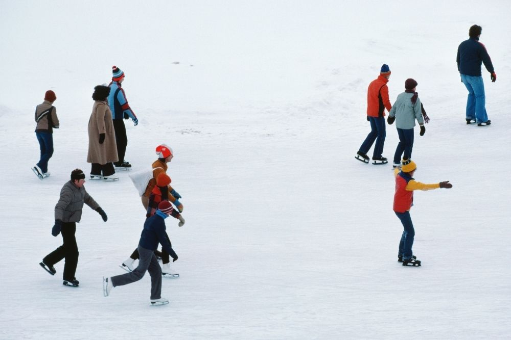 People ice skating outdoors as a traditional form of active winter fitness.