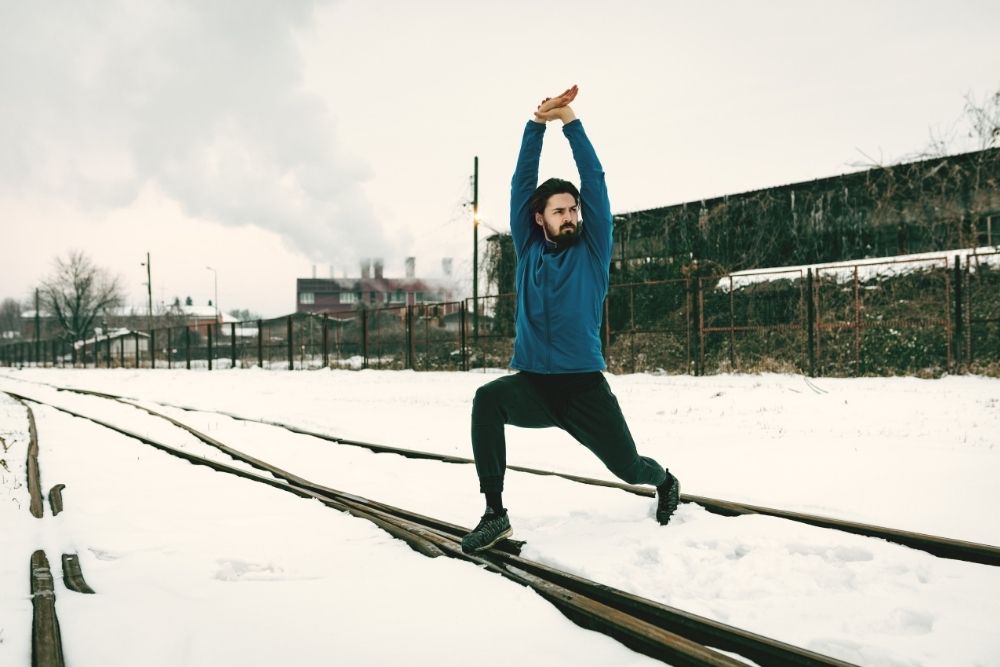 A man stretching in the snow to prepare his body for winter fitness success.