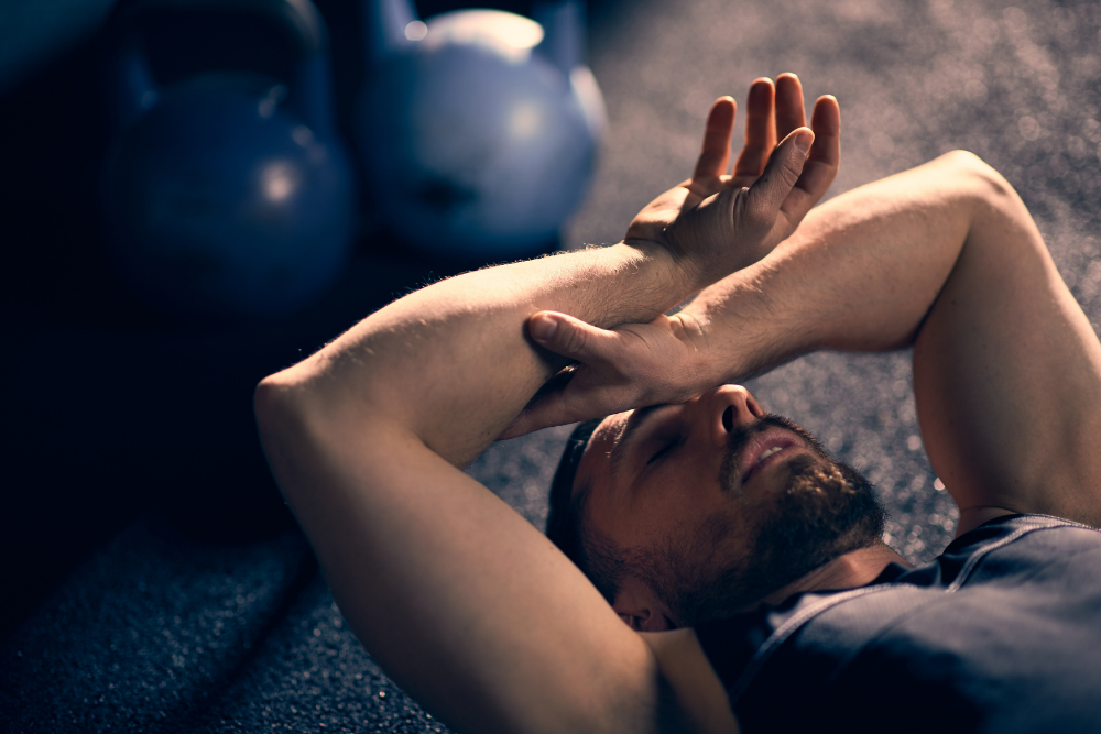 A man lying on the gym floor looking exhausted and humbled after a challenging workout session.