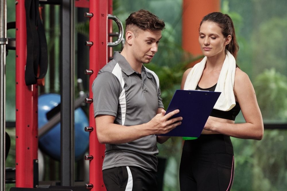 A professional coach discussing a customized pain-free exercise plan with a female client after a movement assessment.
