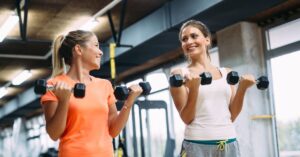 Two women enjoying a pain-free exercise session together in a bright, modern gym setting.