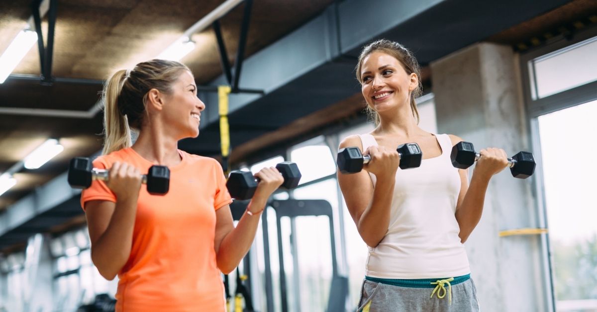 Two women enjoying a pain-free exercise session together in a bright, modern gym setting.