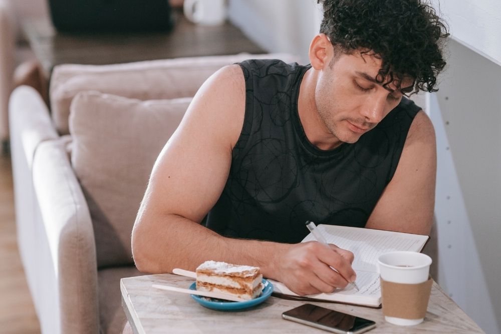 A person writing in a notebook next to a cup of coffee, representing the practice of tracking patterns and building self-awareness.