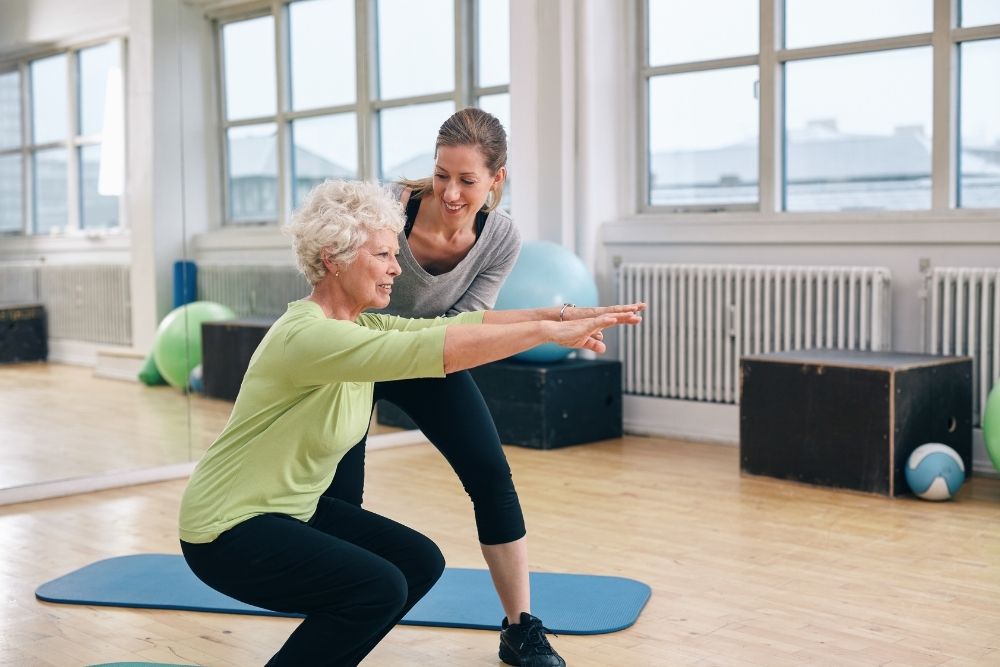 An older woman performing a supervised squat, redefining aging.
