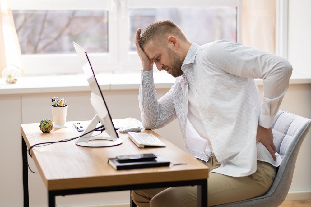 A man in an office, slouching with back pain.