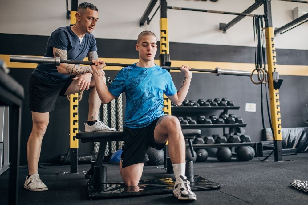 A coach guiding an athlete through strength training exercises in a gym.