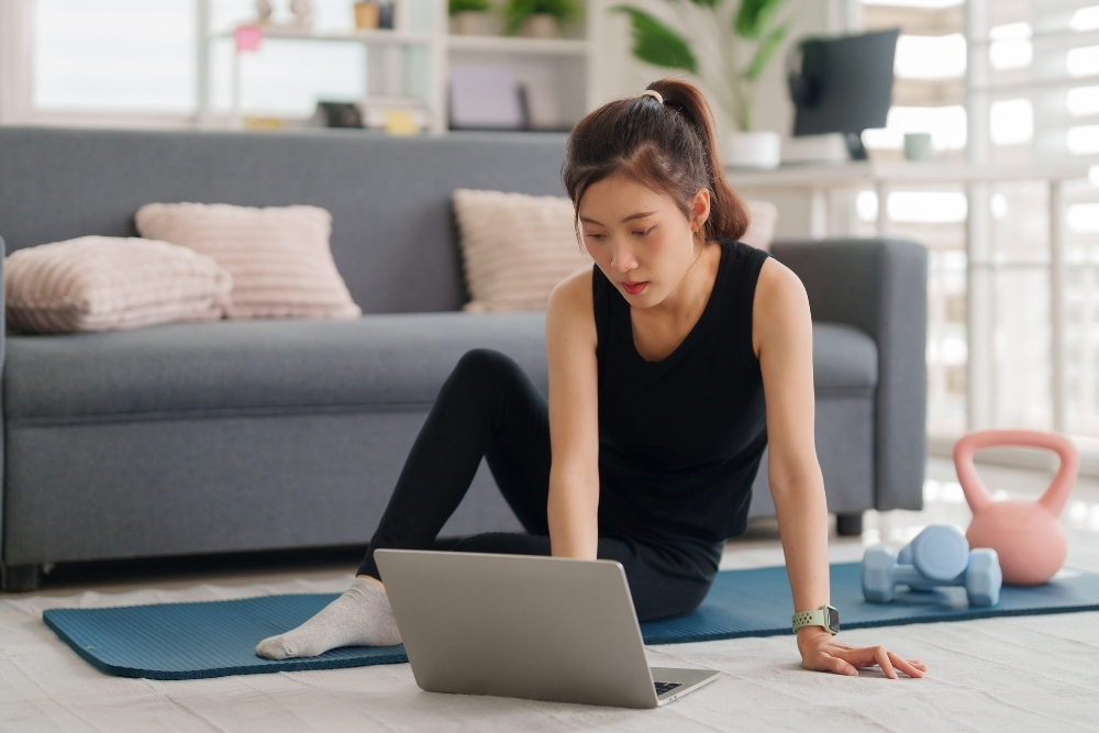 A woman exercising at home with a laptop, showcasing the flexibility and independence of online fitness programming.