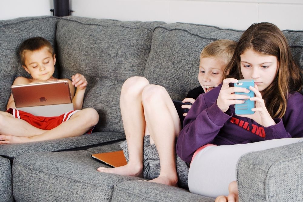Children sitting on a couch focused on their screens, representing the sedentary habits.