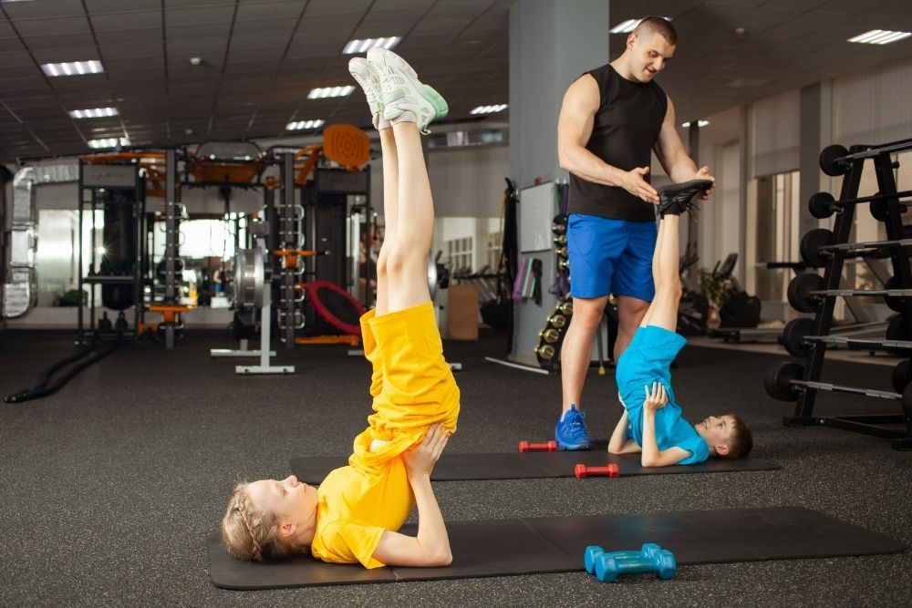 A trainer assisting kids with foundational movement and bodyweight exercises as part of a youth and teens fitness program.