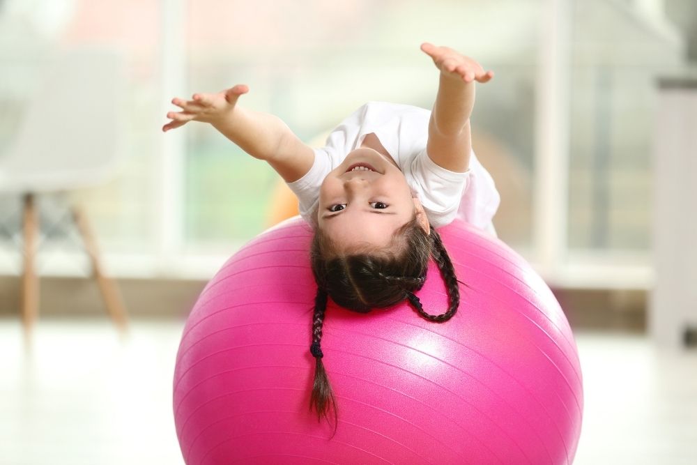 A young girl having fun and playing on a pink exercise ball